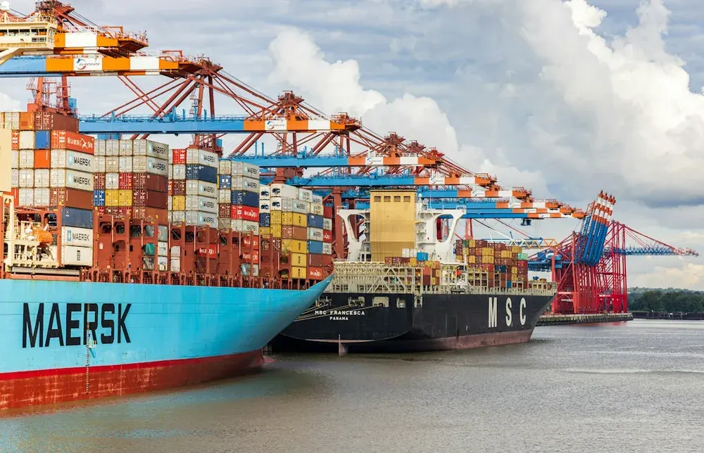 Container ships docked beneath cargo cranes at a port terminal.