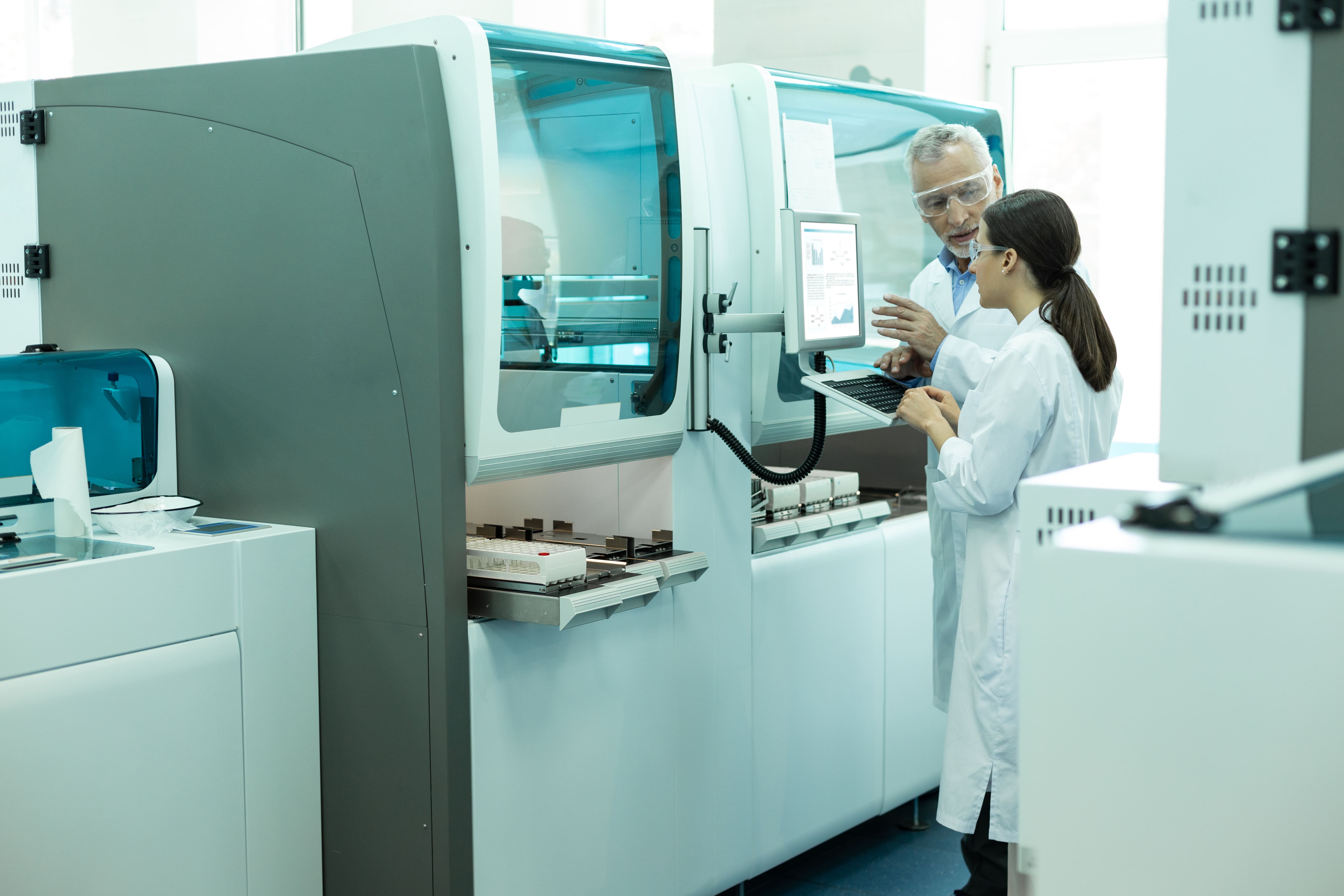 Laboratory specialists reviewing test evidence beside automated testing equipment.